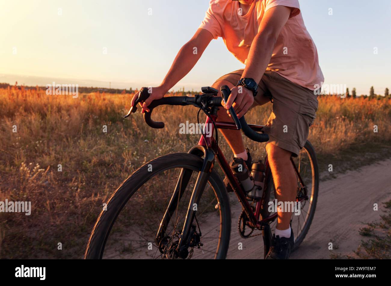 Radfahrer, der bei Sonnenuntergang auf einem Feld fährt. Mann auf dem Fahrrad bei Sonnenuntergang aus nächster Nähe. Aktives Lifestyle-Konzept. Stockfoto