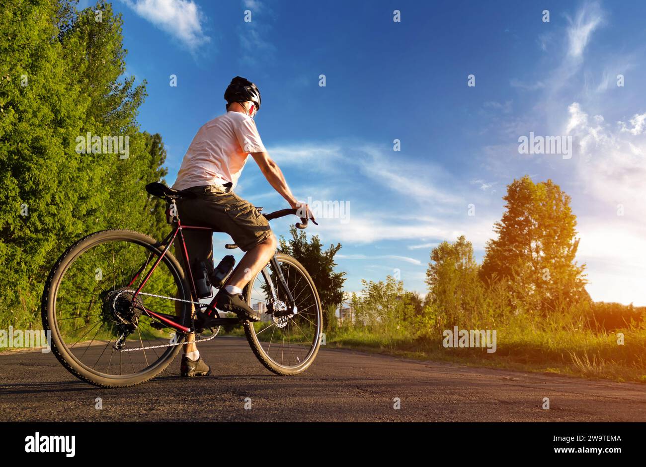 Radfahrer stehen bei Sonnenuntergang auf der Straße. Wunderschöne Landschaft eines Mannes mit Rennrad vor dem blauen Himmel. Sportlicher Lifestyle. Stockfoto