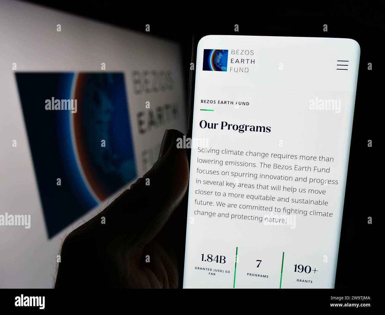 Person, die ein Handy hält, mit Webseite der Umweltorganisation Bezos Earth Fund vor dem Logo. Konzentrieren Sie sich auf die Mitte des Telefondisplays. Stockfoto