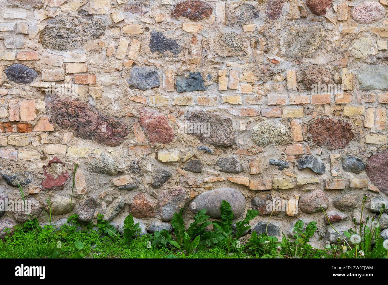 Wandstruktur mit alten Ziegelsteinen, gemischt mit freiliegenden runden Steinen. Hintergrund der Mauerstruktur aus Ziegeln und Stein. Stockfoto