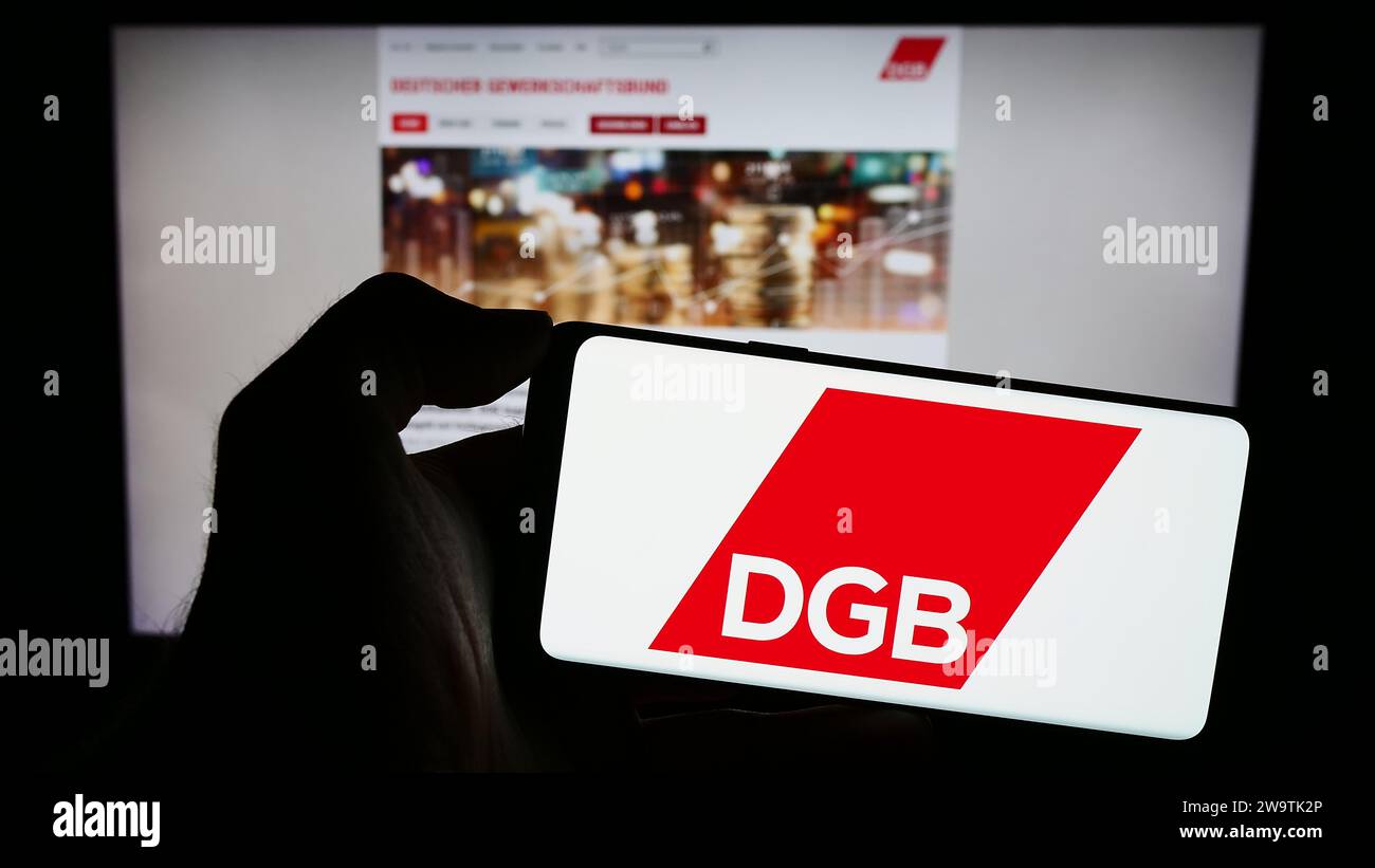 Handybesitzer mit Logo des Deutschen Gewerkschaftsbundes (DGB) vor der Webseite. Schwerpunkt auf dem Display des Telefons. Stockfoto