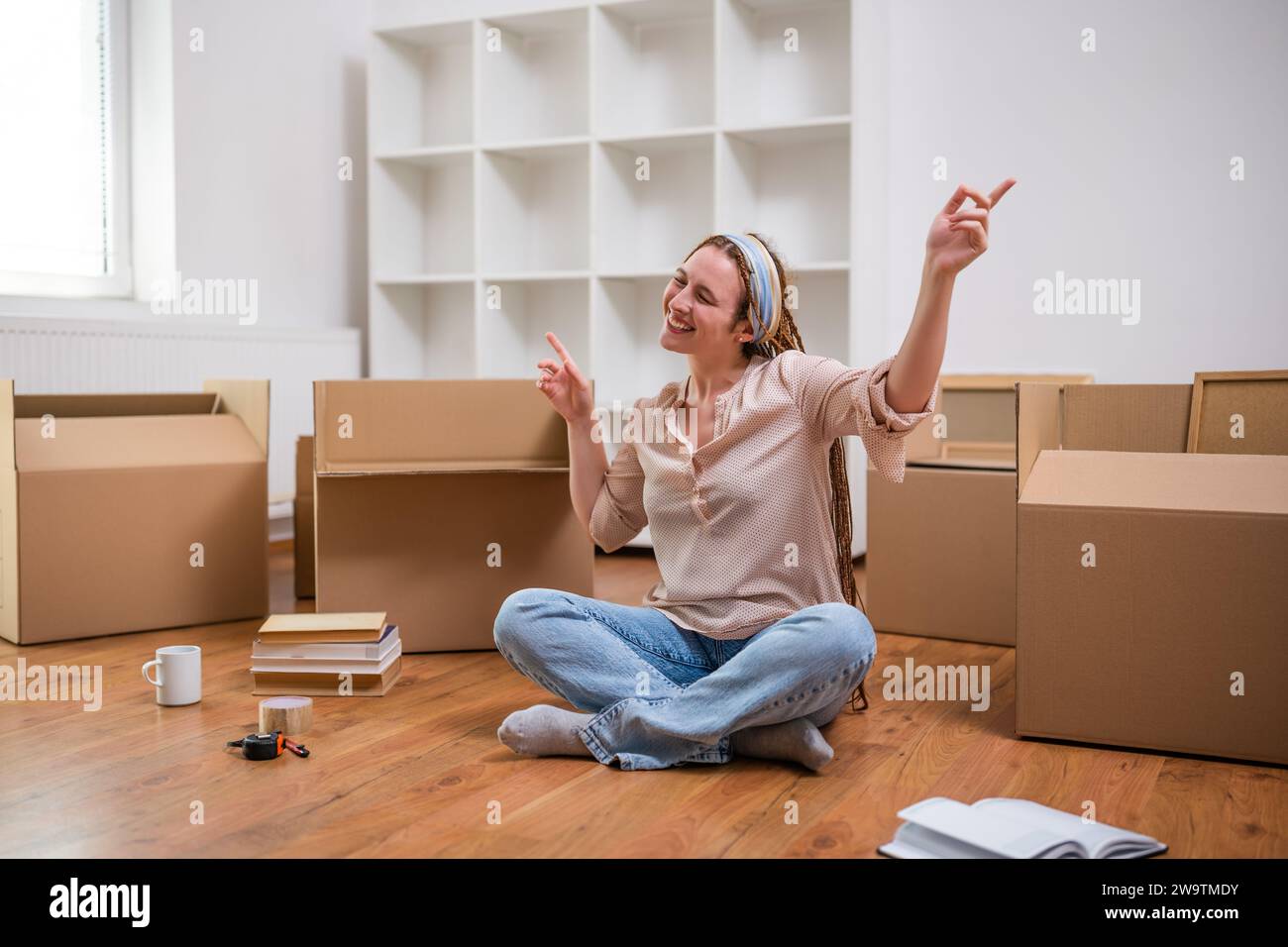 Aufgeregte Ingwerfrau mit Zöpfen zieht in neue Wohnung. Stockfoto