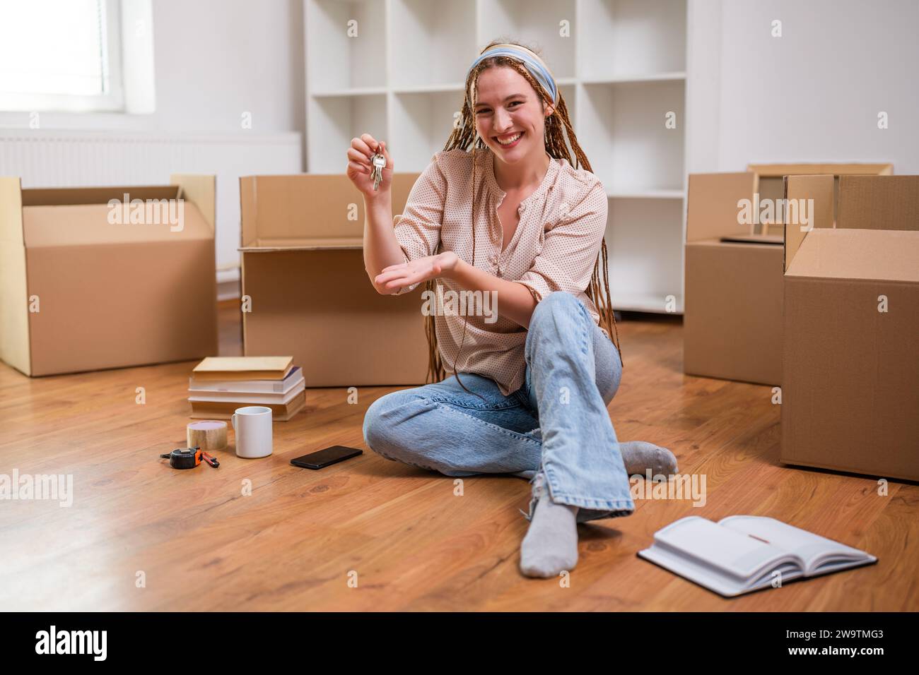 Moderne Ingwerfrau mit Zöpfen, die den Schlüssel zu ihrem neuen Zuhause zeigen. Stockfoto