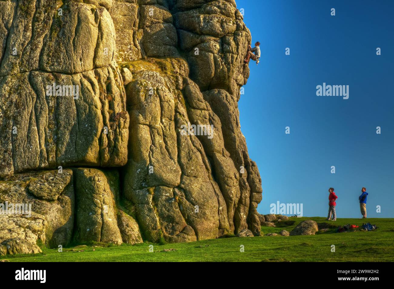 Ein Kletterer auf Haytor Dartmoor mit zwei Klettergefährten, die vom Boden aus beobachten. Stockfoto