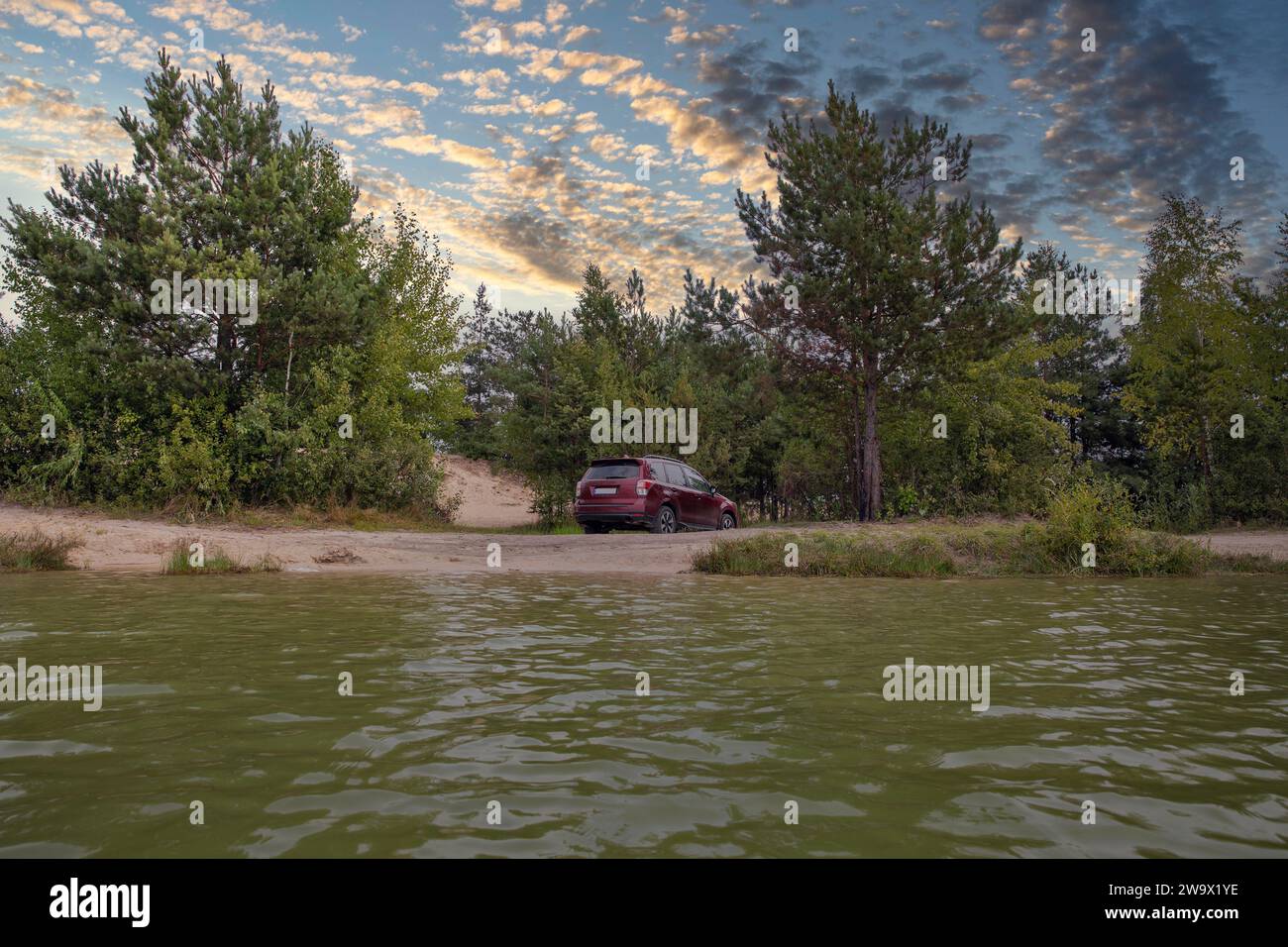 Roter SUV-Wagen in einer Sandgrube im Wald am See. Stockfoto