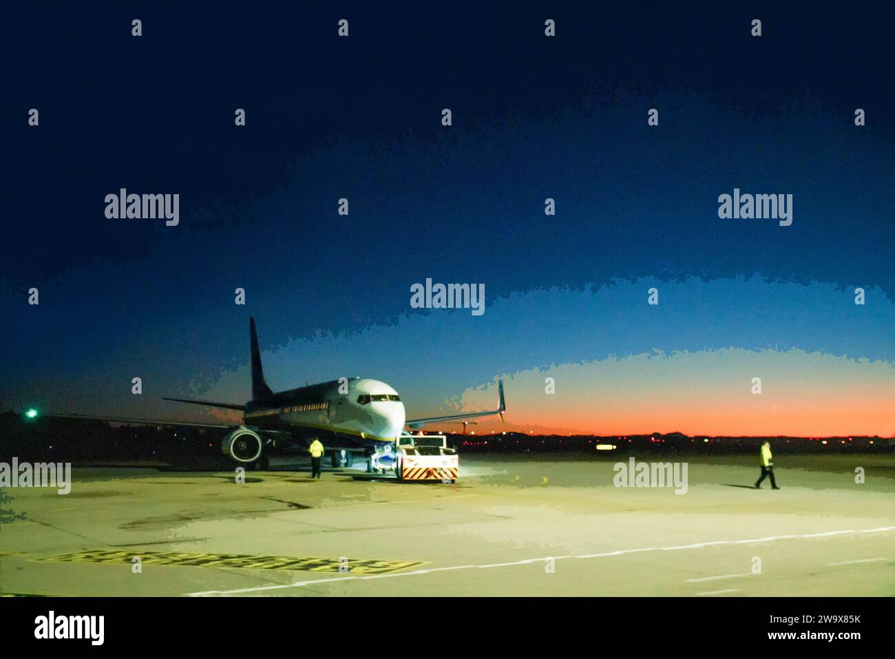 Flughafen Memmingen - Traktor schiebt ein Flugzeug und Techniker (unscharfe Bewegung ) auf Beton in dämmerung Stockfoto