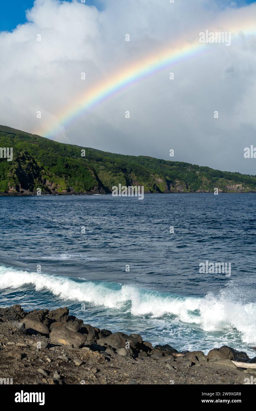 Fangen Sie einen beeindruckenden Regenbogen über der dynamischen Brandung und felsigen Küste entlang der Piilani Autobahn im Haleakalā Nationalpark auf Maui ein. Stockfoto