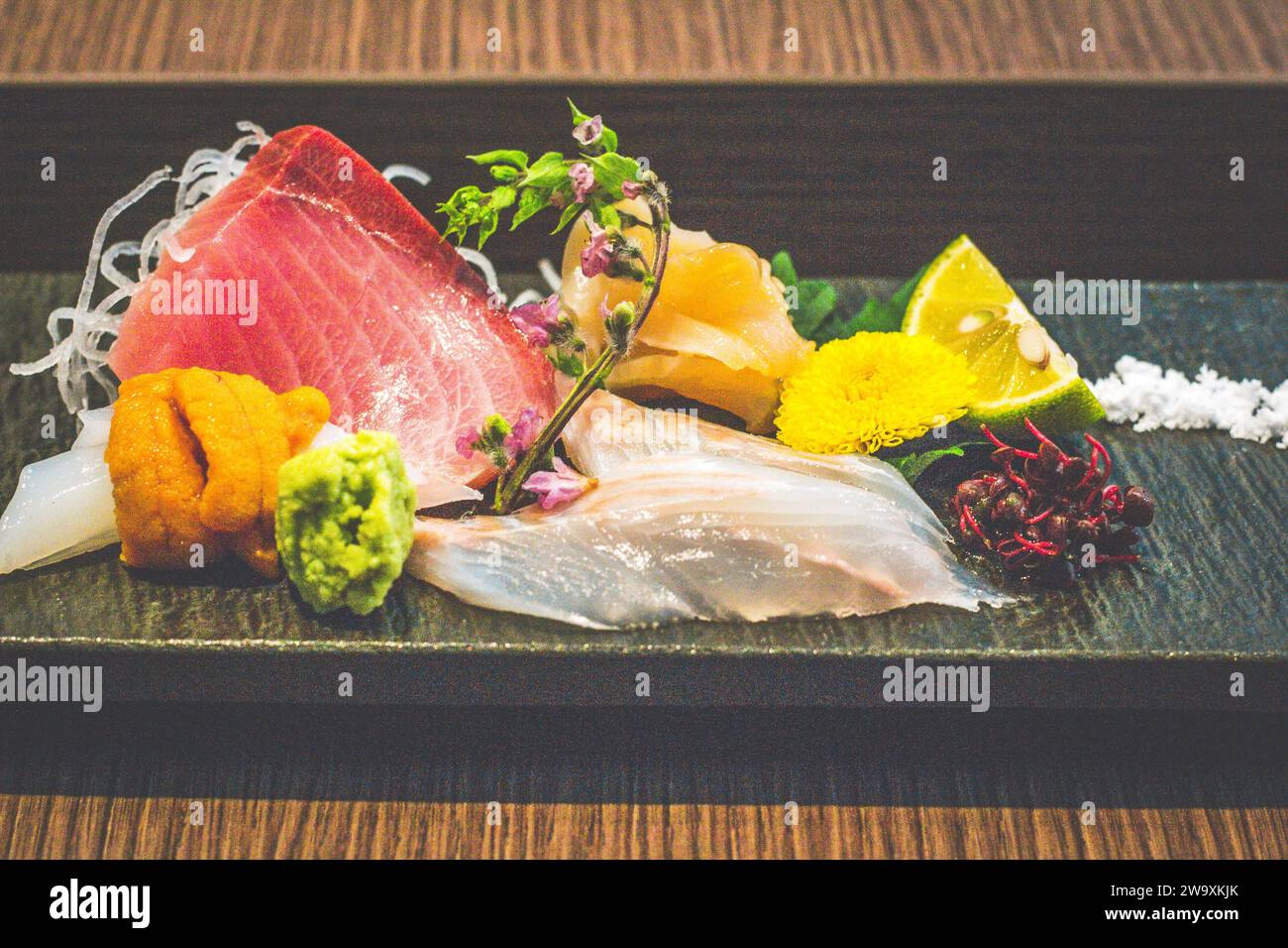 Ein Gericht mit rohem Sashimi-Fisch einschließlich Thunfisch, Tintenfisch, Uni, Seeigel, Wasabi und essbaren Blumen Stockfoto