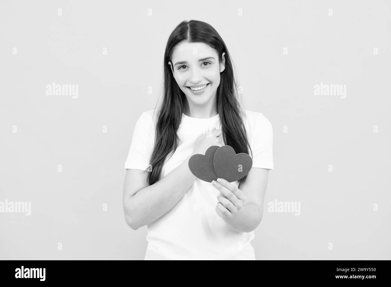 Portrait von schönen süßen niedlichen hübschen Mädchen halten roten Papier Karte Herz isoliert über gelben Hintergrund. Schönes Mädchen hält Herz, Liebe Form. Stockfoto