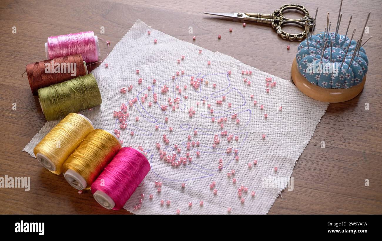 Crafting Harmony: Perlenstickerei-Projekt mit Seidenfäden auf Holztisch Stockfoto