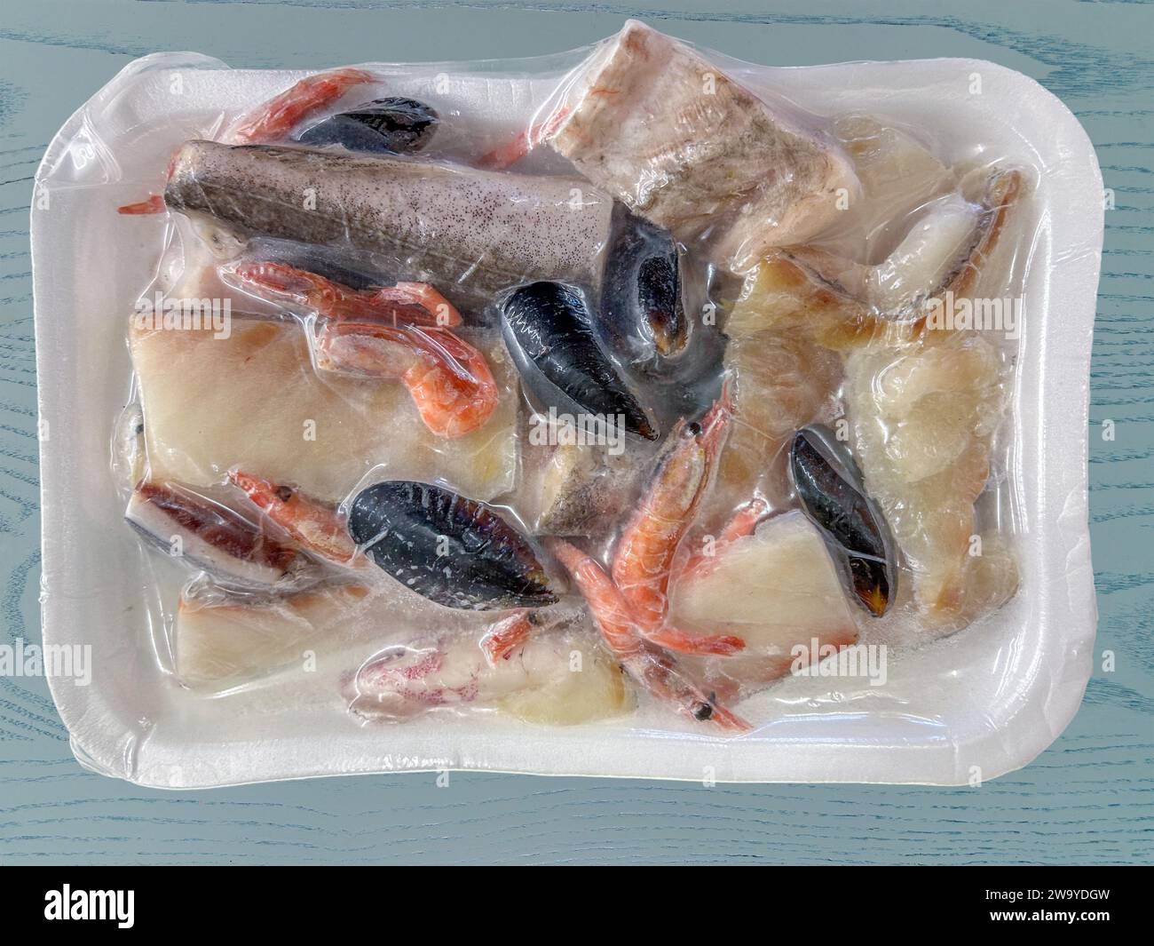 Gemischter, gereinigter und geschnittener Fisch, fertig zum Kochen in Stücken gefroren in vakuumversiegeltem Tablett auf blauem Holzboden mit Schneidepfad, Ansicht von oben Stockfoto