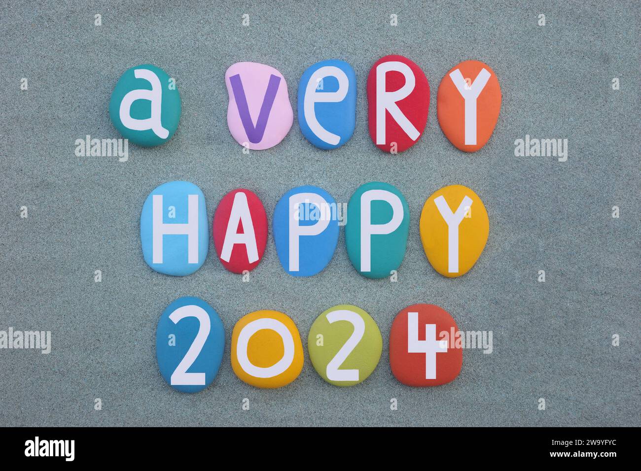 Ein sehr glückliches 2024, das mit handgemalten mehrfarbigen Steinbuchstaben und Zahlen über grünem Sand komponiert wurde Stockfoto