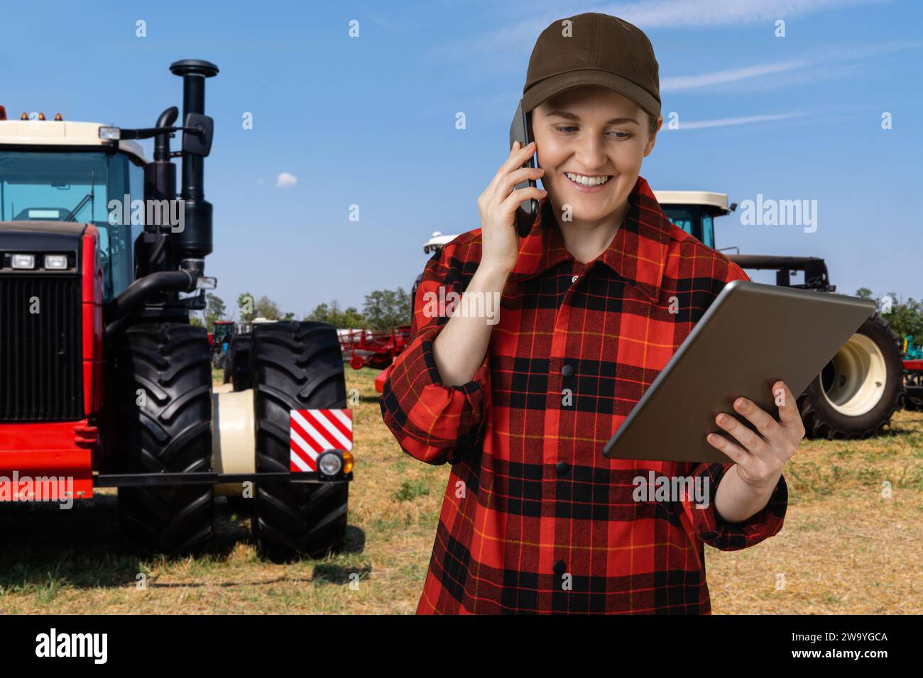 Landwirtin mit einem digitalen Tablet neben einem landwirtschaftlichen Traktor. Stockfoto