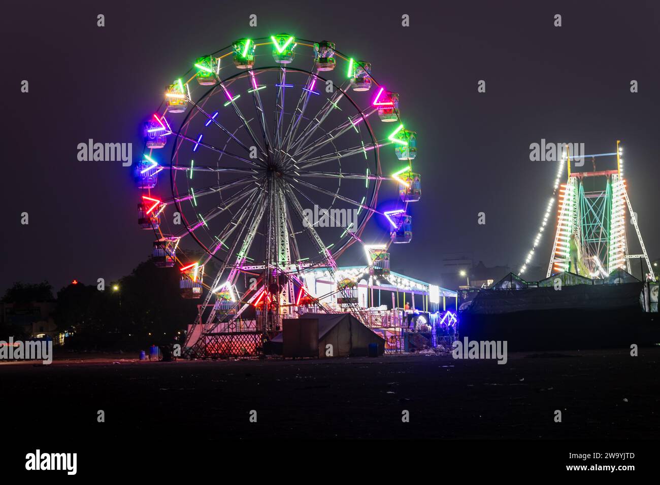 fröhliche Runde Schaukel bei Nacht mit farbenfrohem Licht auf dem Messegelände der Stadt aus verschiedenen Blickwinkeln Stockfoto