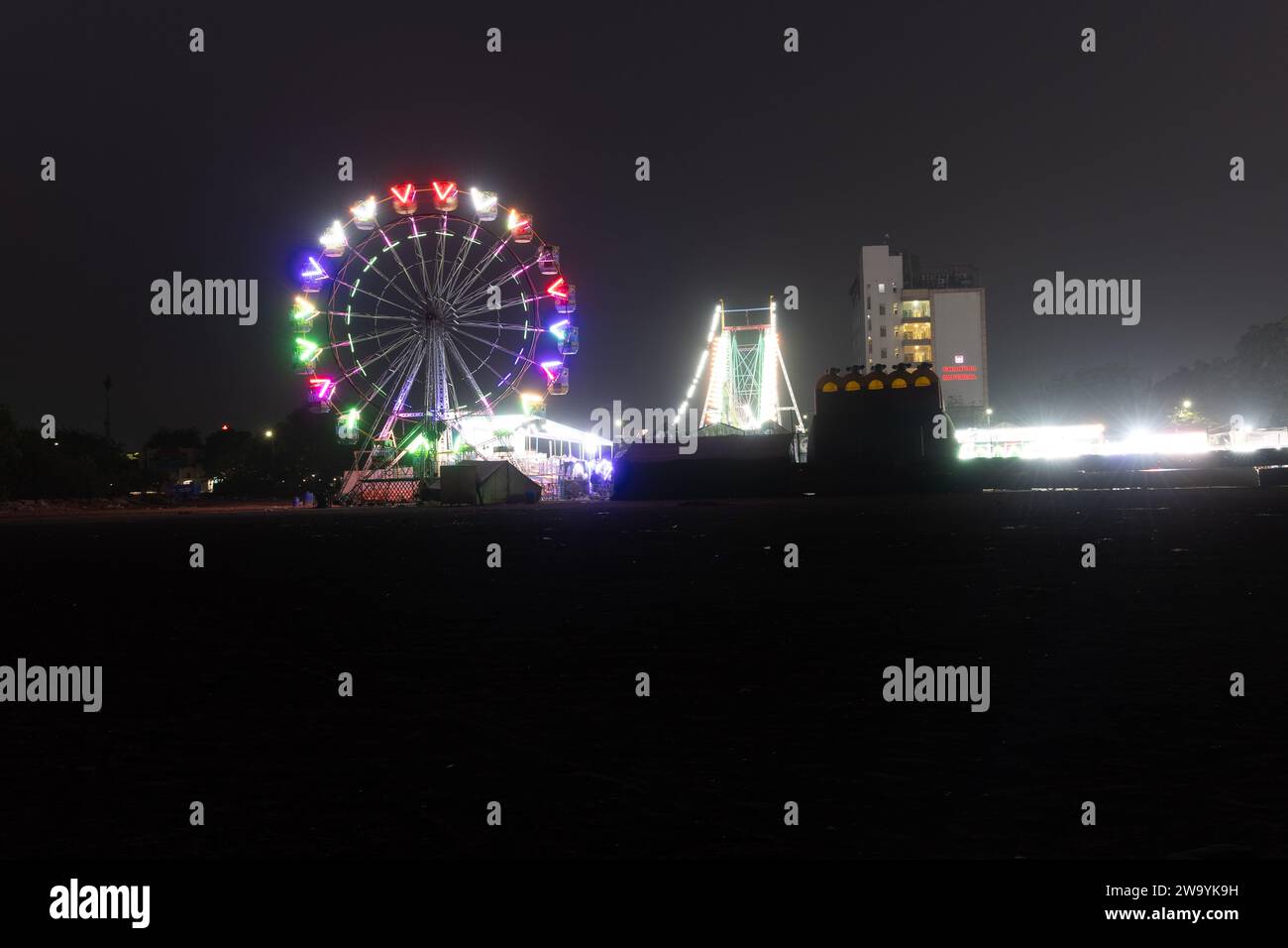fröhliche Runde Schaukel bei Nacht mit farbenfrohem Licht auf dem Messegelände der Stadt aus verschiedenen Blickwinkeln Stockfoto