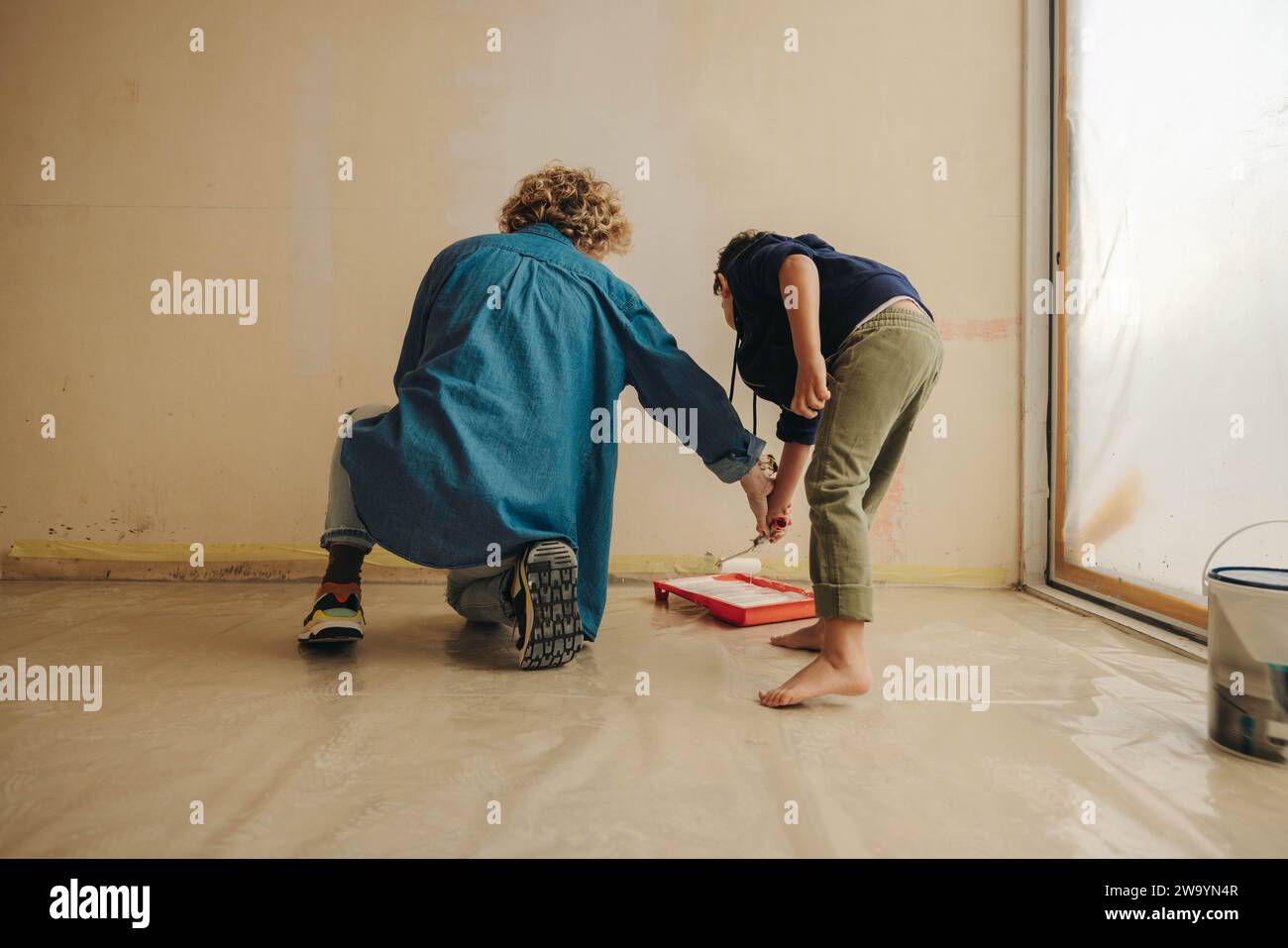 Kreative, kaukasische Mutter und ihr junger Sohn malen zusammen eine Innenwand und renovieren ihr Haus. Dieses DIY-Projekt zeigt ihr Engagement für Stockfoto