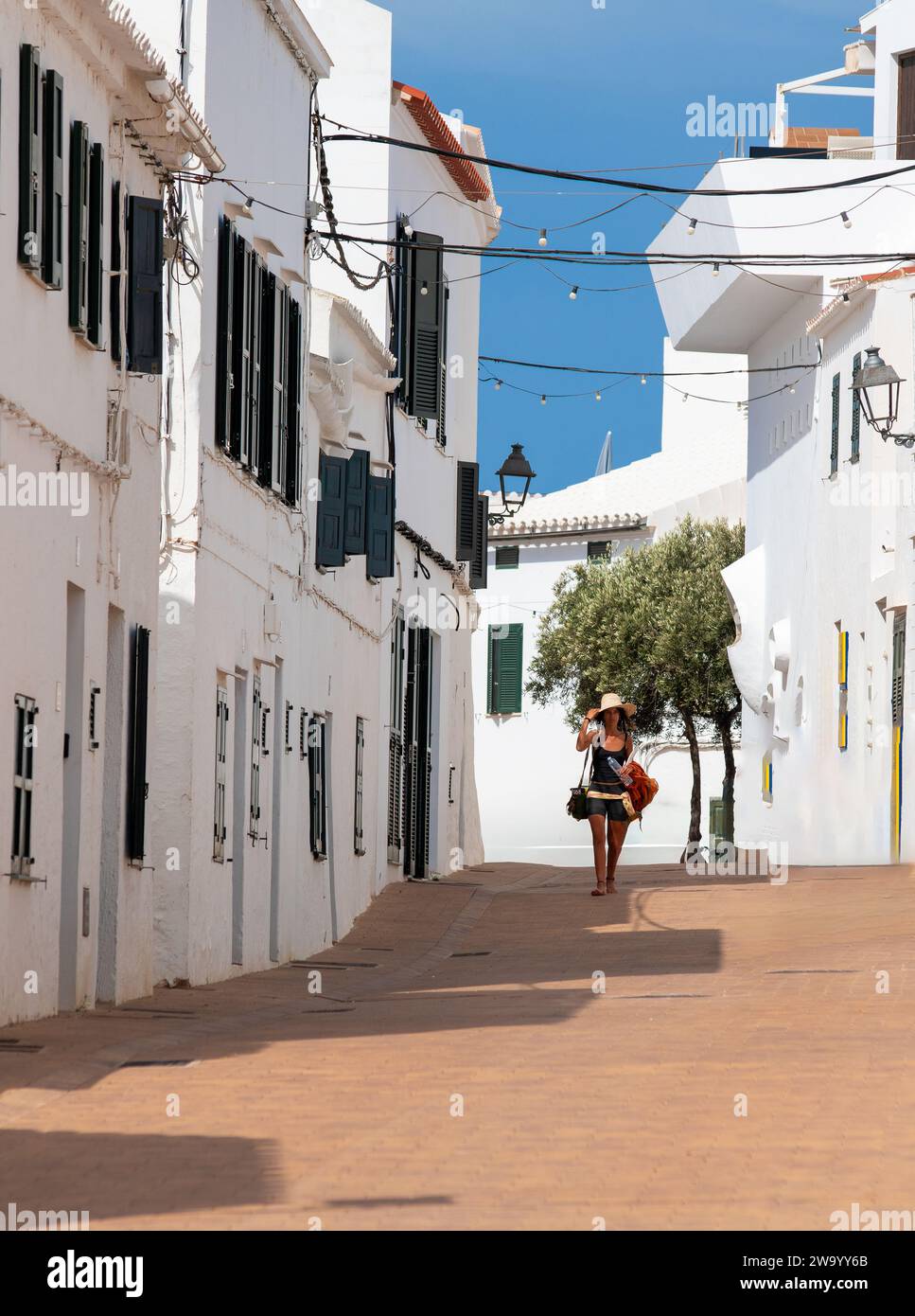 Eine Frau mit Sonnenhut, die eine Straße in Fornells Menorca Spanien entlang läuft. Stockfoto