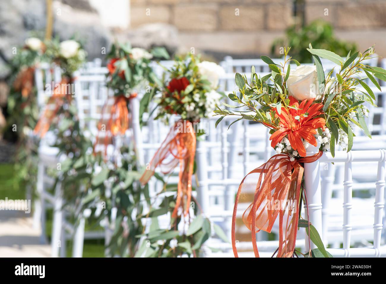 Weiße Holzstühle, dekoriert mit Blumen und üppigem Grün als Teil einer Hochzeitszeremonie, akribische Vorbereitung des Außenbereichs Stockfoto