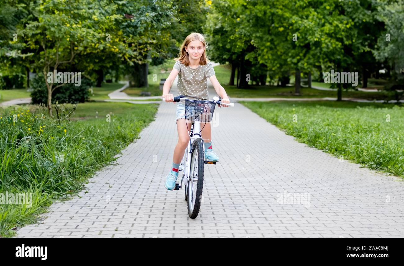 Niedliches junges Mädchen, das im Freien auf dem Fahrrad reitet und in der wunderschönen europäischen Stadt lächelt. Hübsches Kind mit Fahrrad auf der Straße Stockfoto