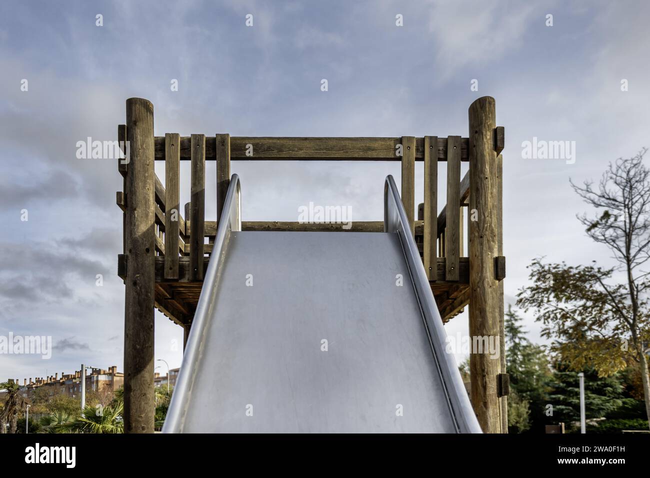 Oben auf einer großen Metallrutsche mit Holzstruktur in einem Kinderspielplatz an einem Tag mit klarem Himmel Stockfoto Oben auf einer großen Metallrutsche mit Holzstruktur in einem Kinderspielplatz an einem Tag mit klarem Himmel Stockfoto