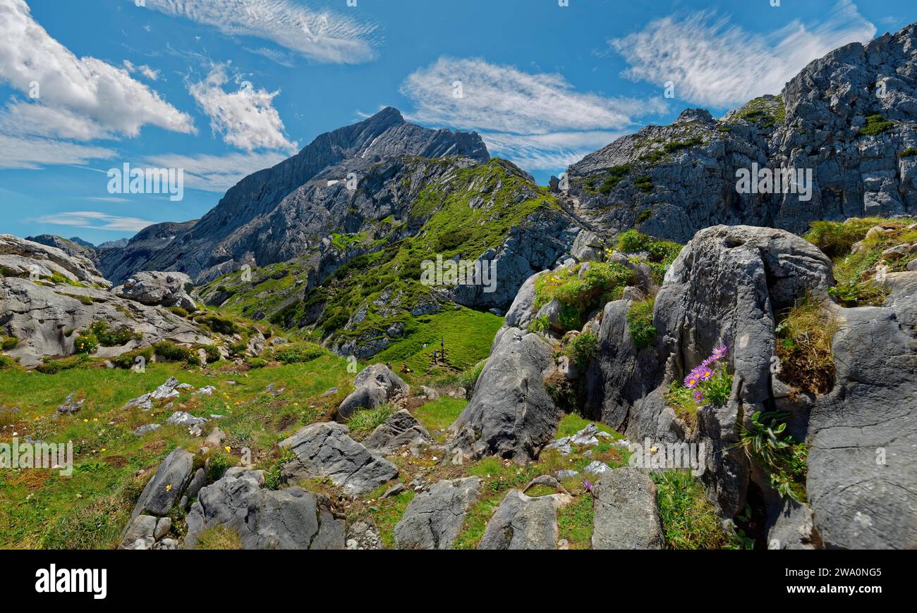 Eine idyllische Berglandschaft mit grünen Wiesen und zerklüfteten Felsen unter blauem Himmel mit Wolken, Panorama, Alpspitze, Osterfelderkopf, AlpspiX, Kreuzeck, Stockfoto