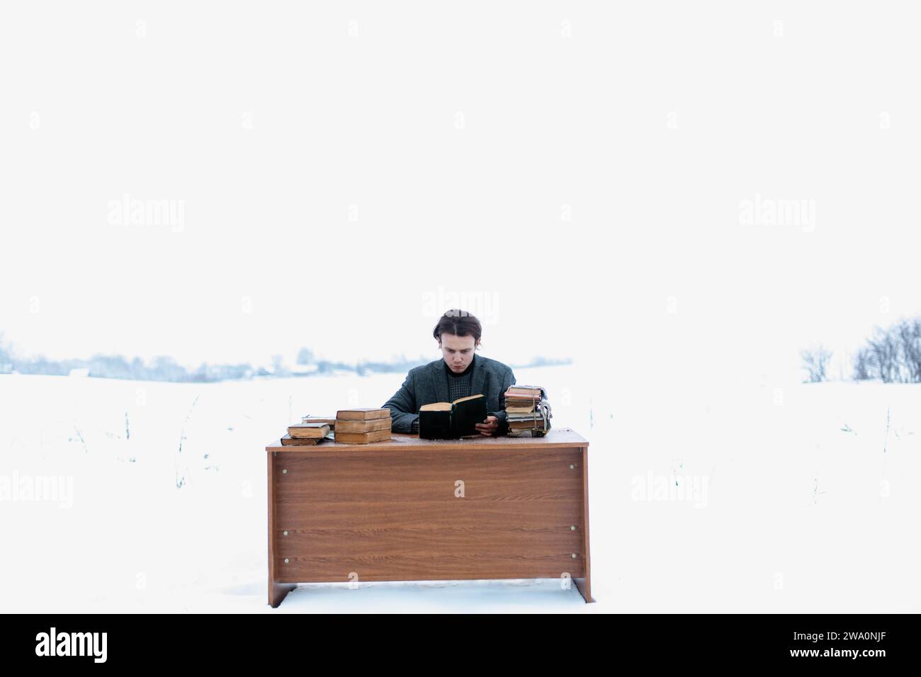 Ein junger, gutaussehender, intelligenter Mann in einer Jacke sitzt an einem Tisch auf einem Feld und liest im Winter alte Bücher Stockfoto