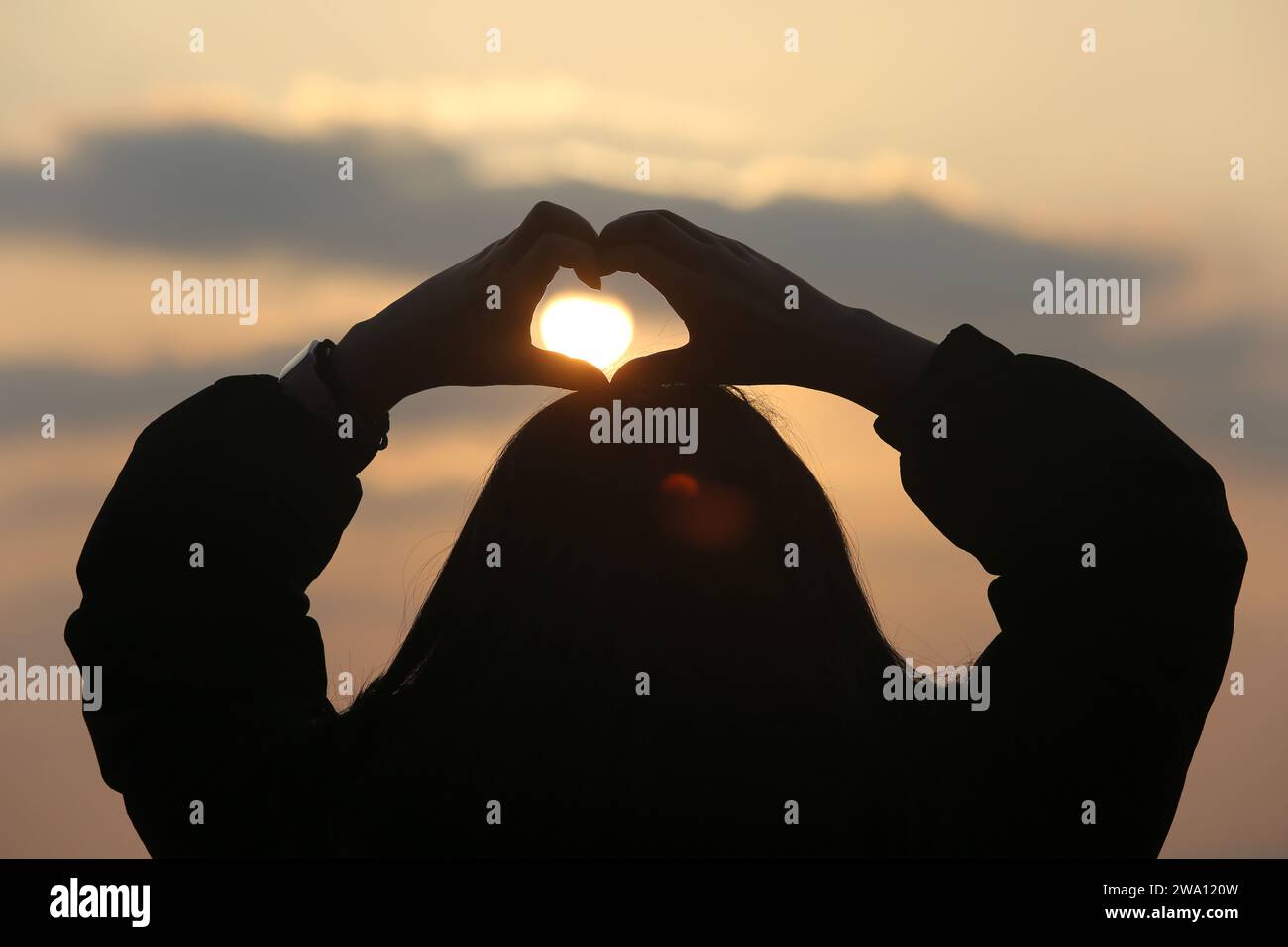 LIANYUNGANG, CHINA - 1. JANUAR 2024 - Ein Mädchen posiert die Herzform für ein Foto mit der aufgehenden Sonne in Lianyungang, Provinz Jiangsu, China, Januar Stockfoto