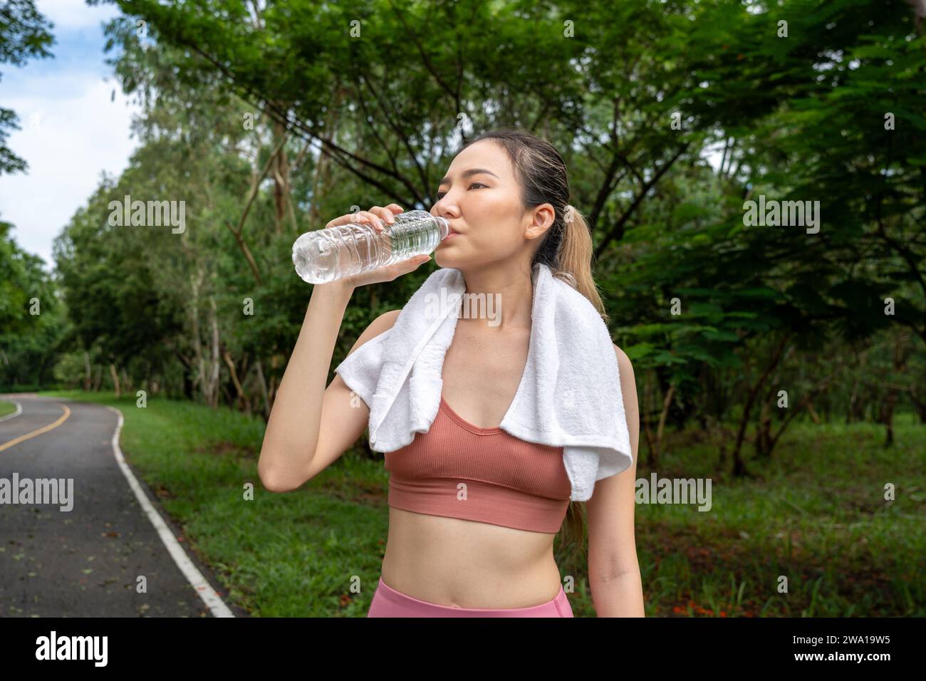 Eine junge asiatische Frau in Fitnesskleidung hält an, um Wasser aus ihrer Plastikflasche zu trinken, während sie morgens auf einer Laufbahn eines Einheimischen trainieren kann Stockfoto