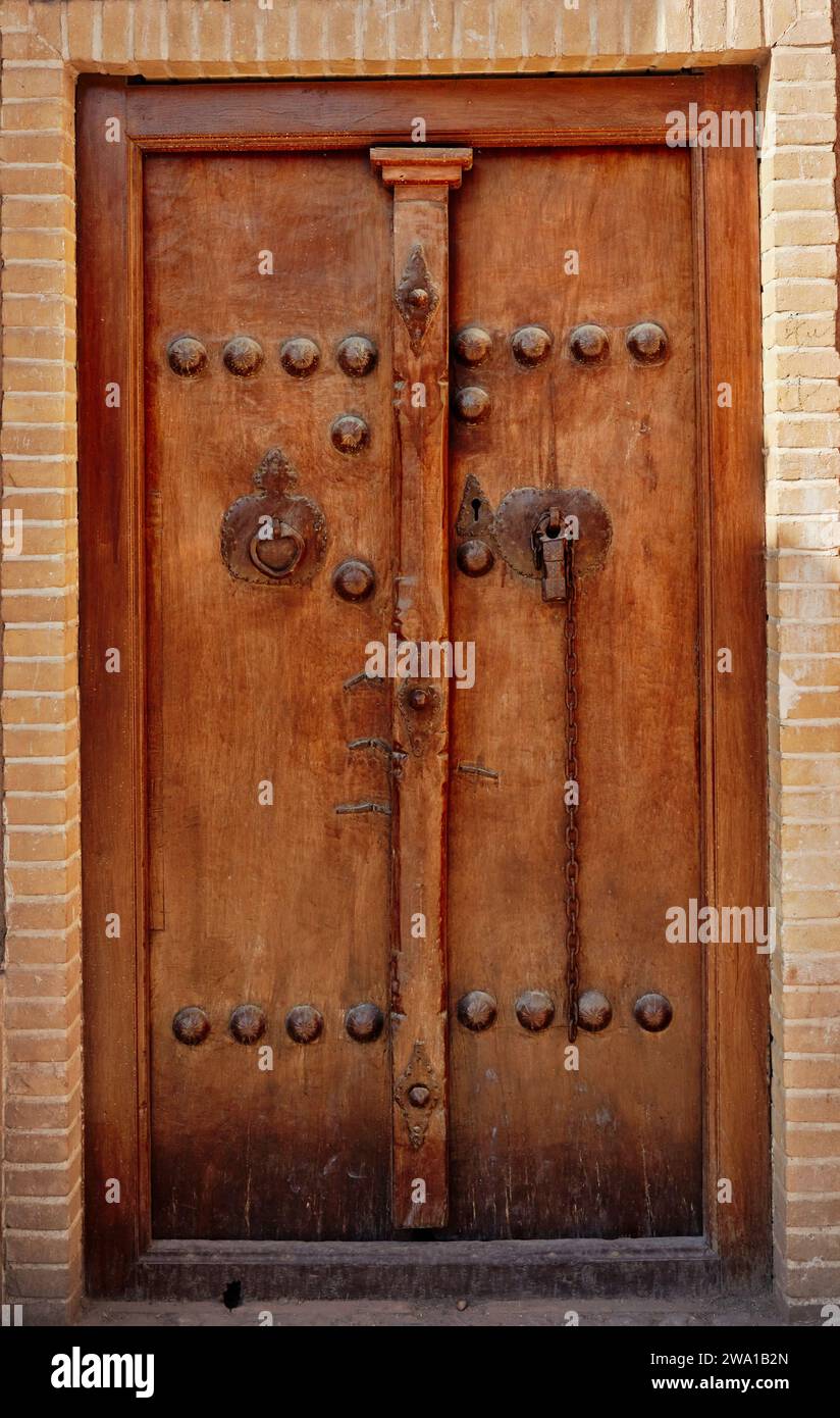 Alte Holztür von Sultan Amir Ahmad Bathhouse mit zwei verschiedenen Klopfern - Metallstab für Männer und Metallring für Frauen. Kaschan, Iran. Stockfoto