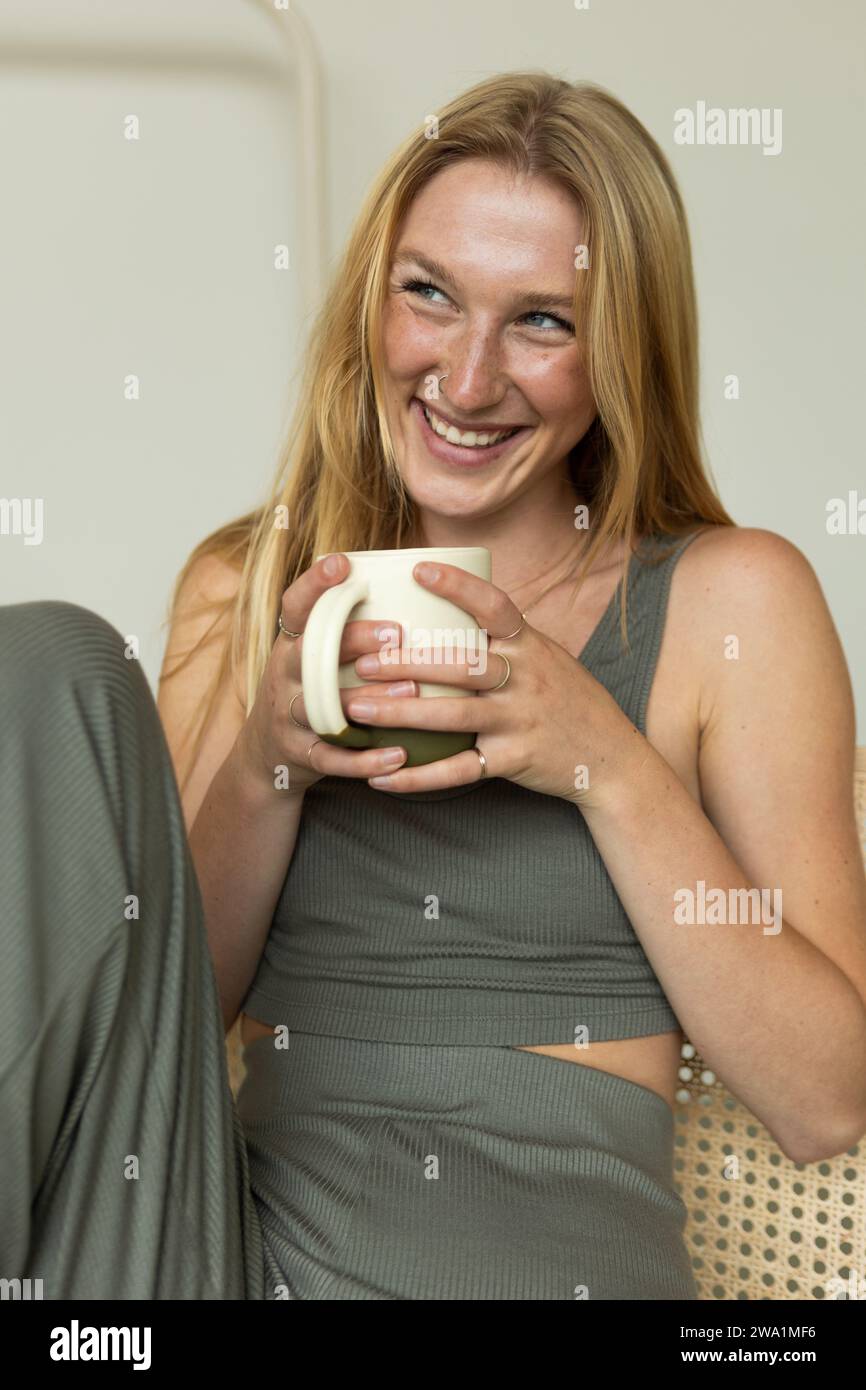 Die lachende junge Frau genießt Morgenkaffee im ruhigen Schlafzimmer Stockfoto