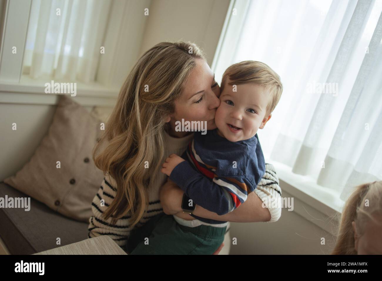 Mutter küsst liebevoll ihre entzückende Kleinkinder-Wange Stockfoto