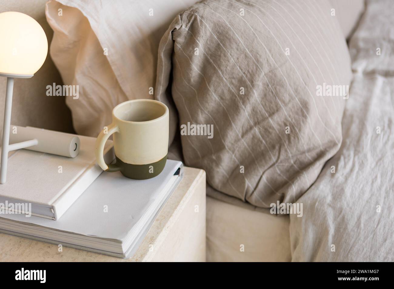 Keramikbecher auf Büchern neben einem ästhetischen Bett schafft eine ruhige Szene Stockfoto