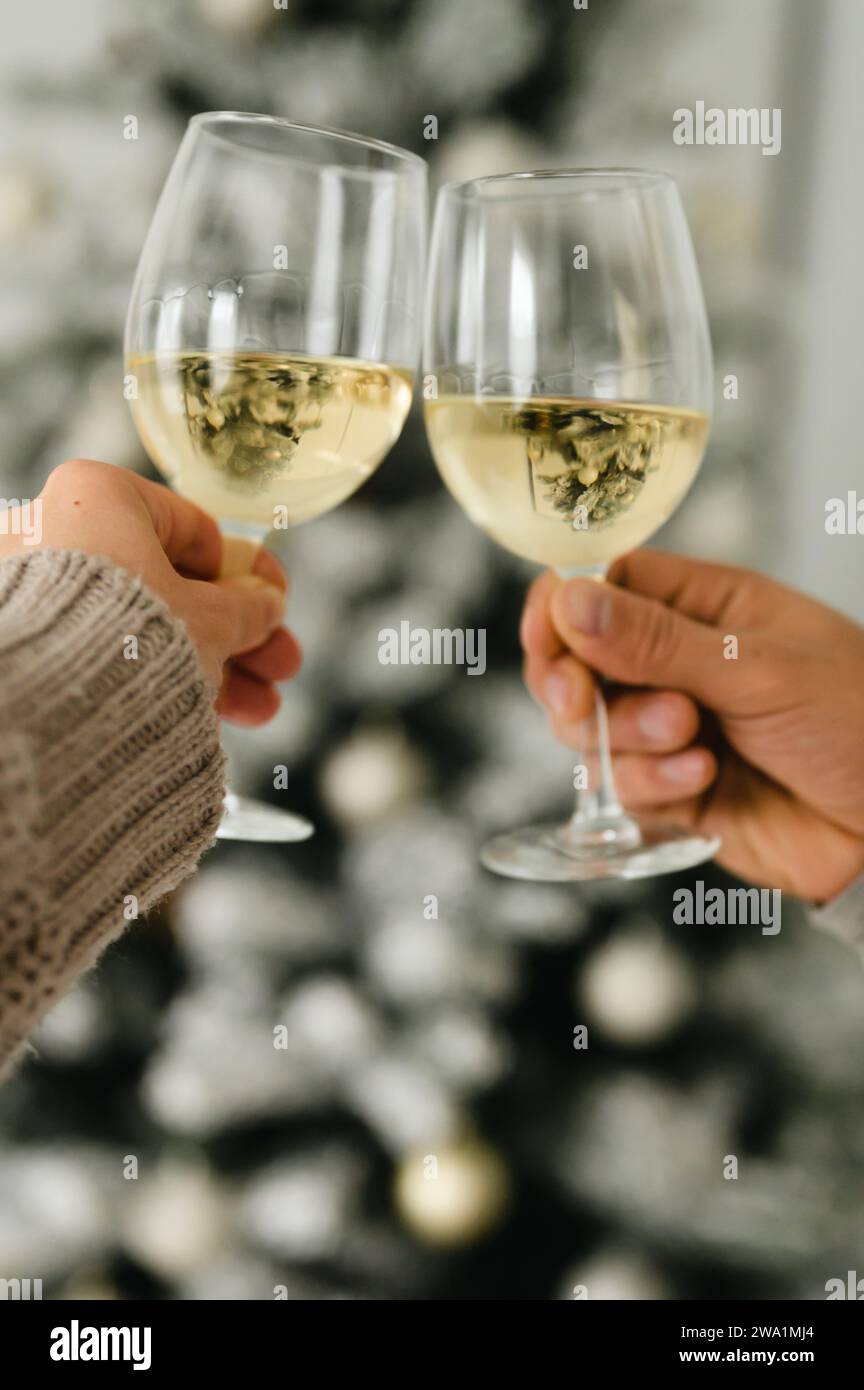 Zwei Leute, die mit Gläsern Wein vor dem weihnachtsbaum jubeln Stockfoto