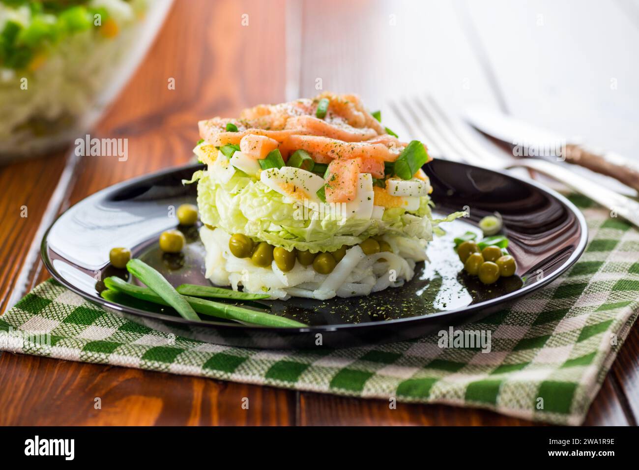 Mehrschichtiger Salat aus Kohl und anderem Gemüse mit rotem Fisch auf einem Teller. Auf einem Holztisch. Stockfoto
