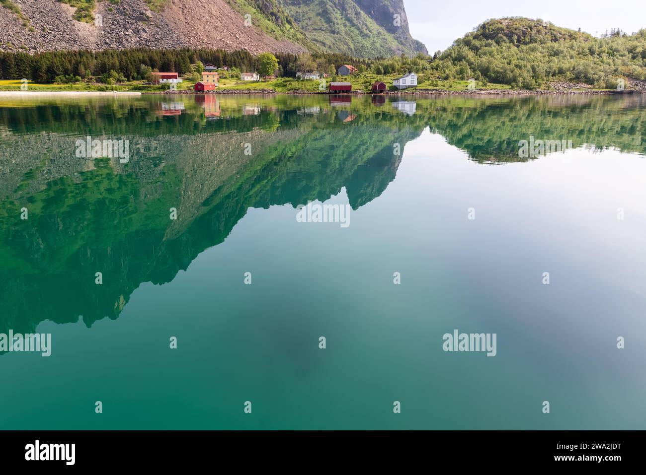 Ein atemberaubender Spiegel im ruhigen Wasser eines Lofoten-Fjords fängt das Sommergrün und die berühmten Rorbu-Hütten des ländlichen Norwegens ein Stockfoto