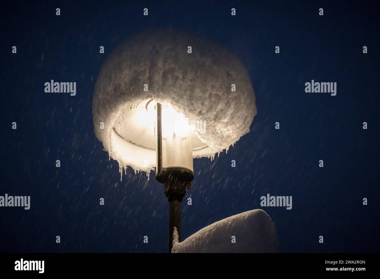 Straßenleuchte mit Motorhaube aus Neuschnee bei starkem Schneefall in der Nacht, Bayern, Deutschland Stockfoto