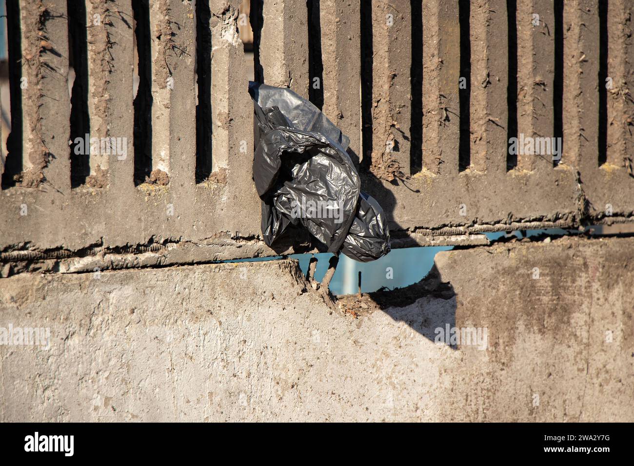 Eine schwarze leere Plastiktüte wiegt tagsüber auf einem Betonzaun in einer Stadt in der Sonne in der Ukraine, Müll, Umweltverschmutzung Stockfoto