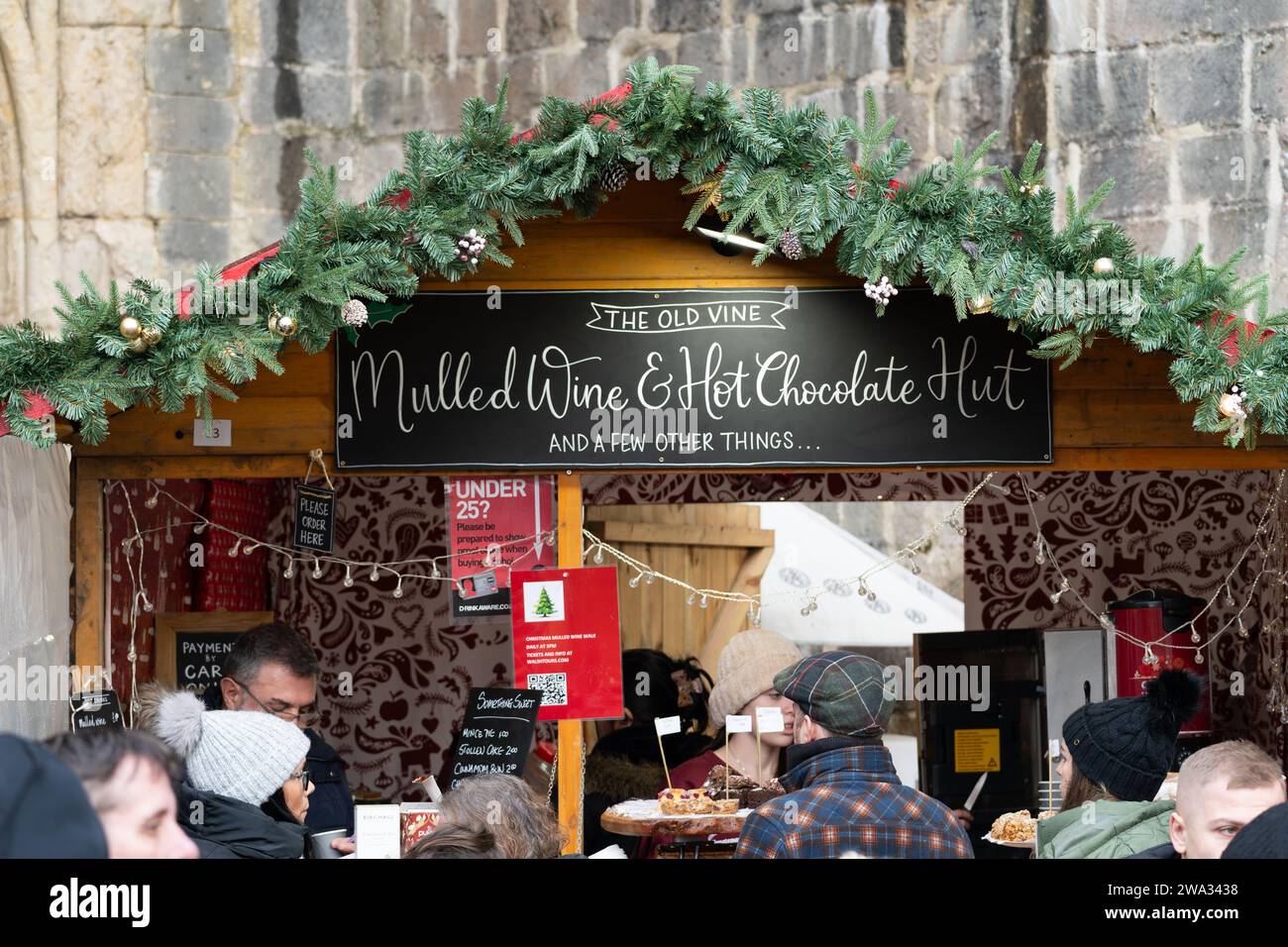 Durstige Gäste, die sich in der Glühweinhütte „The Old Vine“ auf dem Weihnachtsmarkt der Winchester Cathedral um Glühwein und heiße Schokolade schlange. England Stockfoto