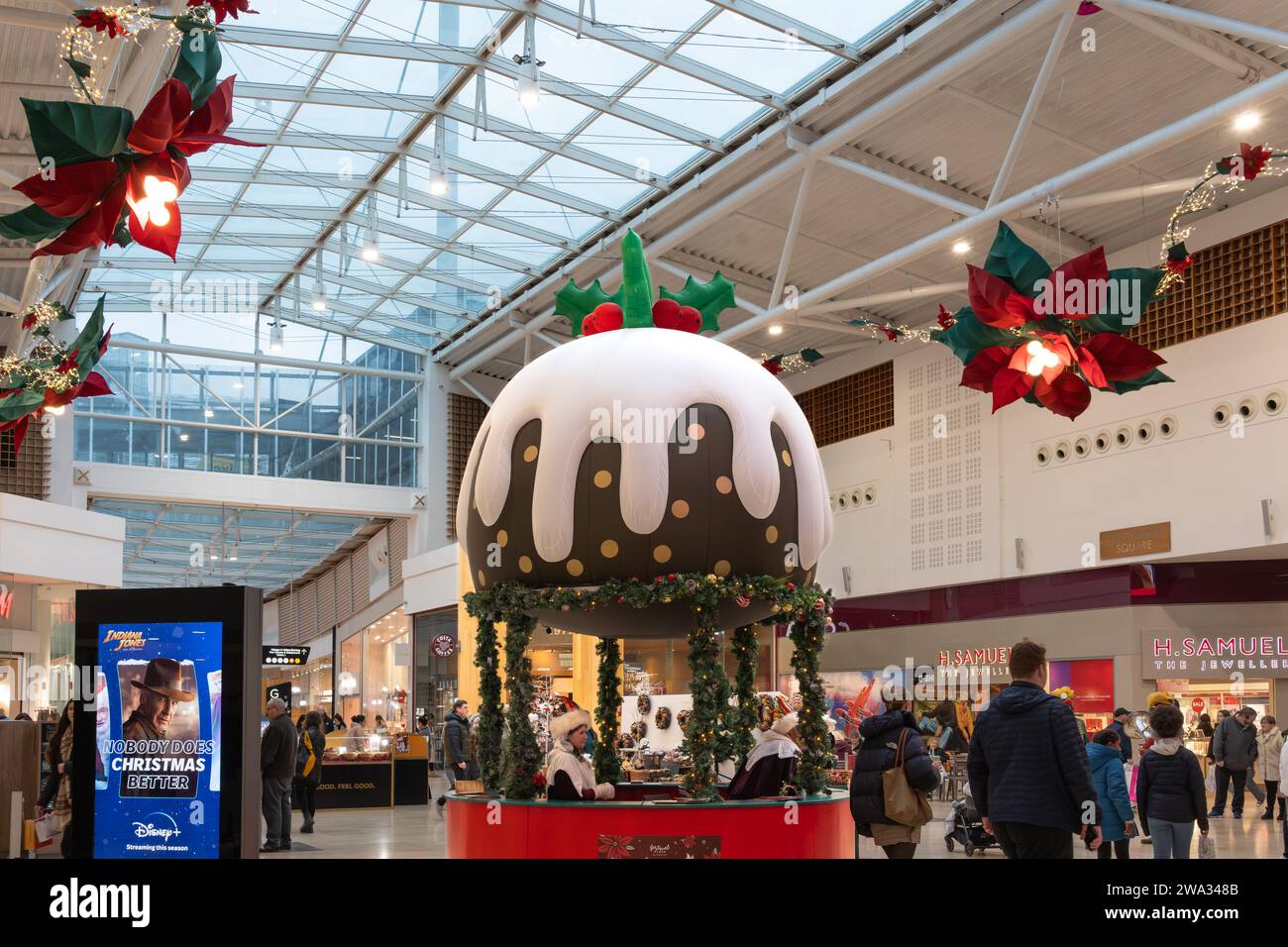 Im Dezember kaufen Shopper Weihnachten am Porchester Square, dem Festival Place, mit einem riesigen Weihnachtspudding-Dekor. Basingstoke, Großbritannien Stockfoto