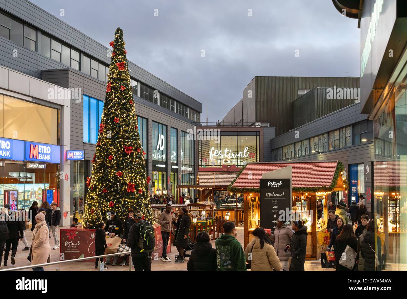 Weihnachtseinkäufer, Marktstände und Weihnachtsbaum im Einkaufszentrum Malls vor dem Festival Place in der Abenddämmerung. Basingstoke, Großbritannien Stockfoto