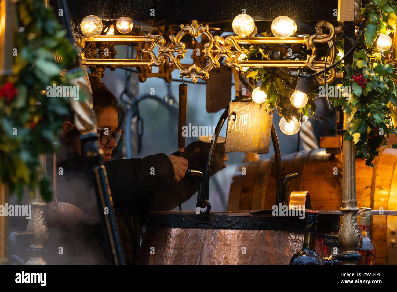 Eine Frau, die Gluhwein (Glühwein) aus einem heißen Kupferkessel auf dem Winchester Cathedral Christmas Market in Hampshire, Großbritannien, in eine Tasse hüllt Stockfoto