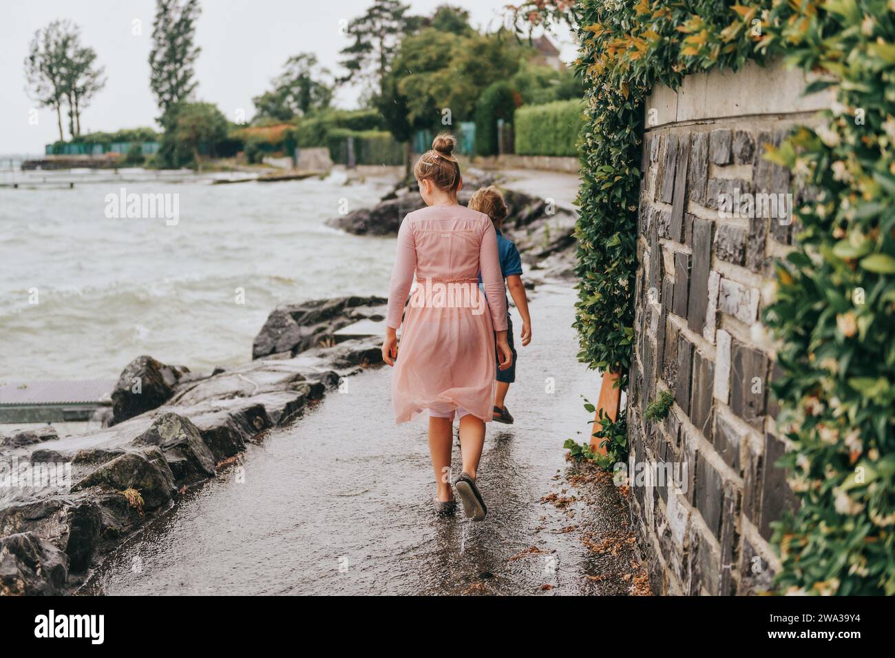 Süße kleine Kinder, die an einem sehr windigen Tag unter Sommerregen am See spielen. Aufnahme am Genfersee, Lausanne, Schweiz Stockfoto