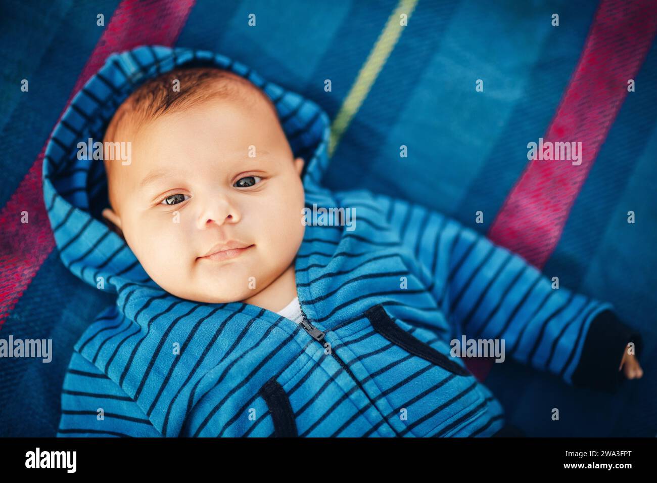 Nahaufnahme Porträt des entzückenden Jungen, der draußen auf dem Cover liegt und eine blaue Streifenjacke trägt Stockfoto