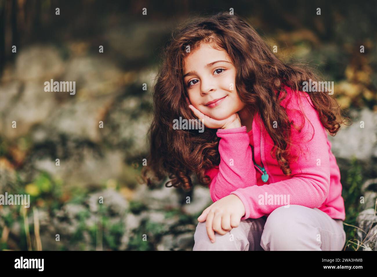 Outdoor-Porträt eines entzückenden kleinen 3-4-jährigen Mädchens mit schönen langen Haaren und rosa Fleecejacke Stockfoto