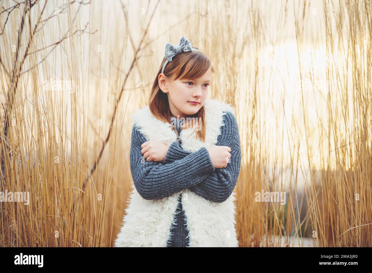 Außenporträt eines süßen 8-9-jährigen Mädchens mit grauem Pullover und weißer Kunstfellweste Stockfoto