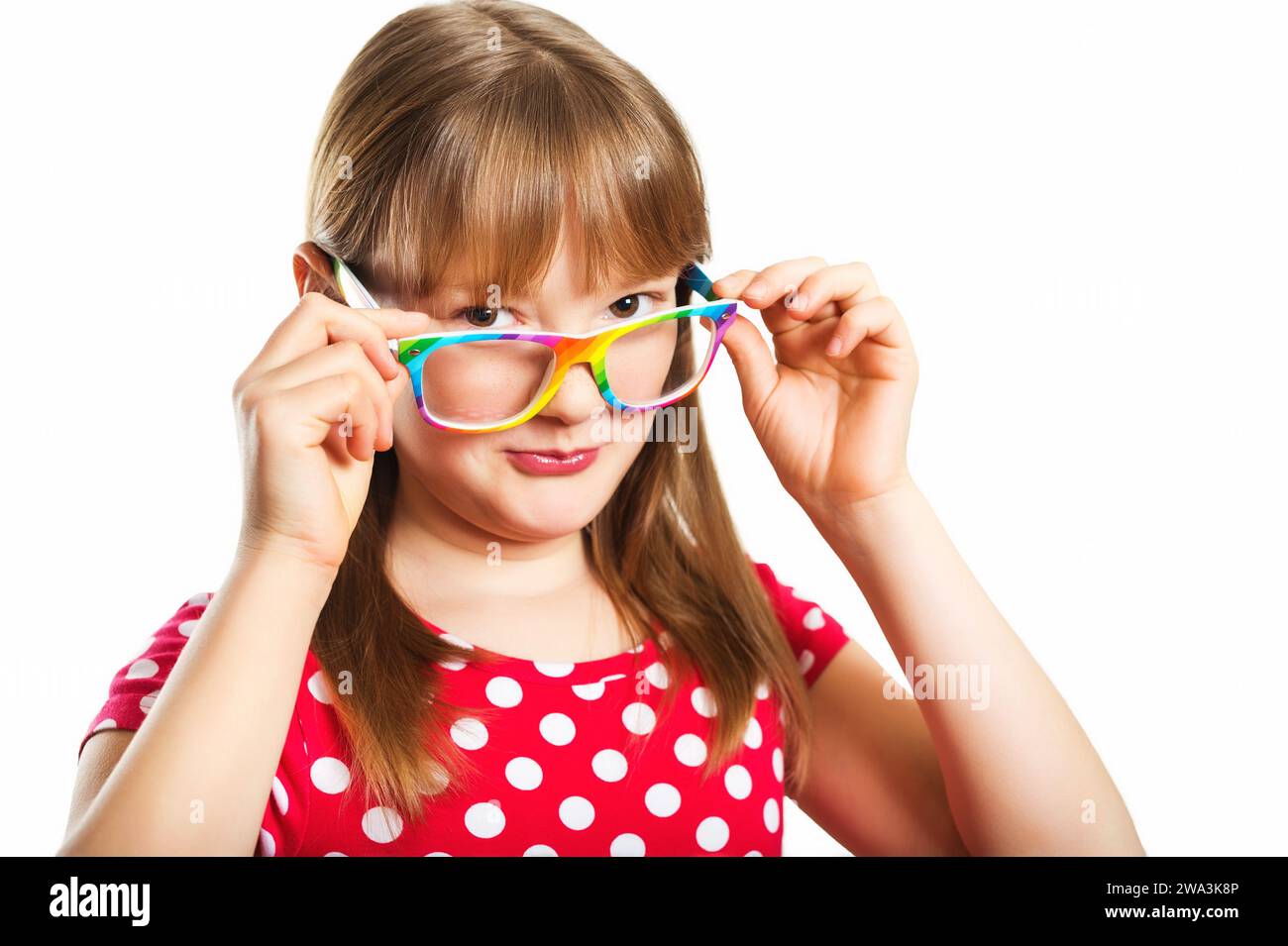 Studio-Porträt des entzückenden kleinen 9-10-jährigen Mädchens, mit Regenbogenbrille und rotem Polka Dot Kleid, stehend vor weißem Hintergrund Stockfoto