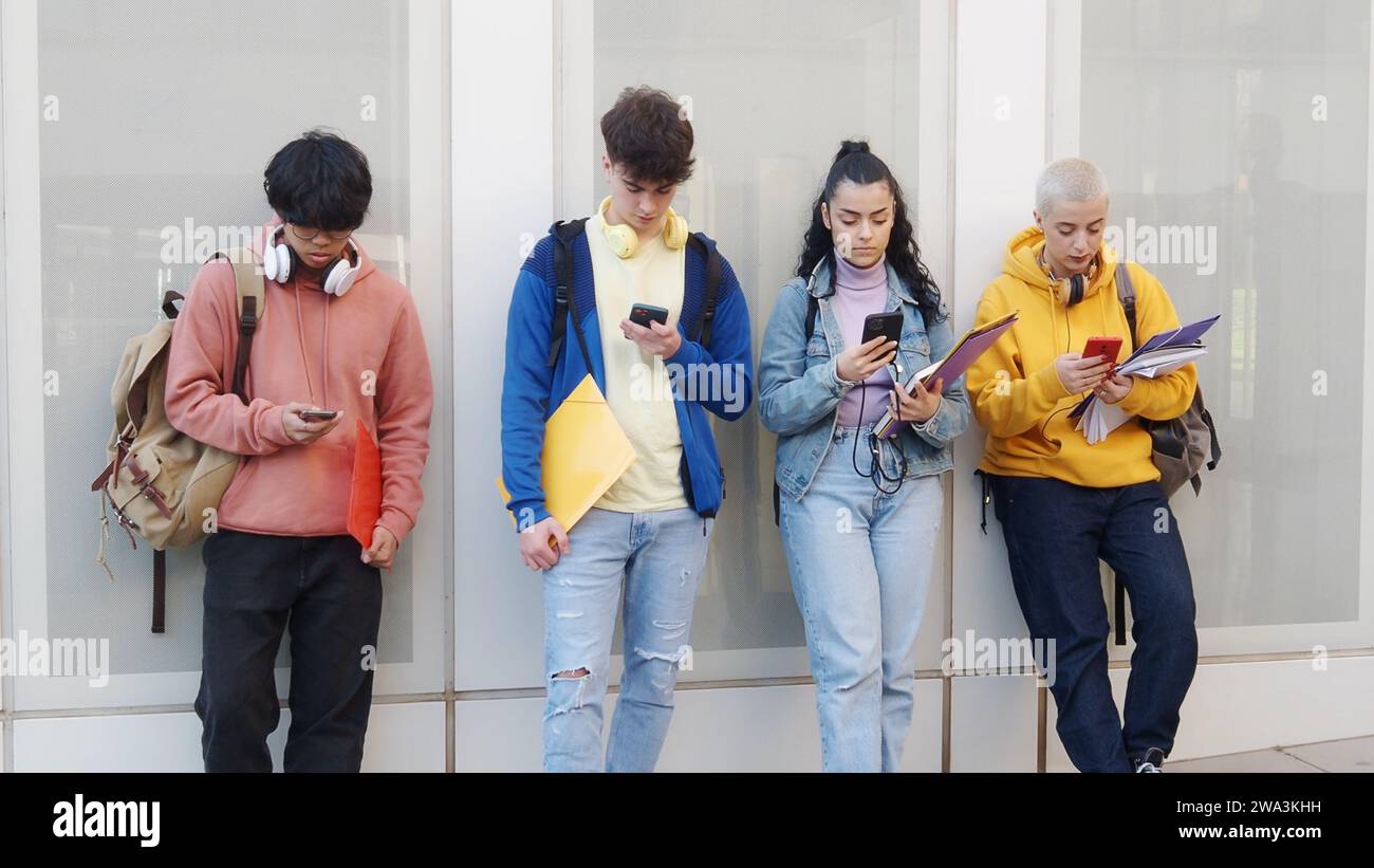 Vier junge Jugendliche, die auf dem Campus ein Smartphone ansehen Stockfoto