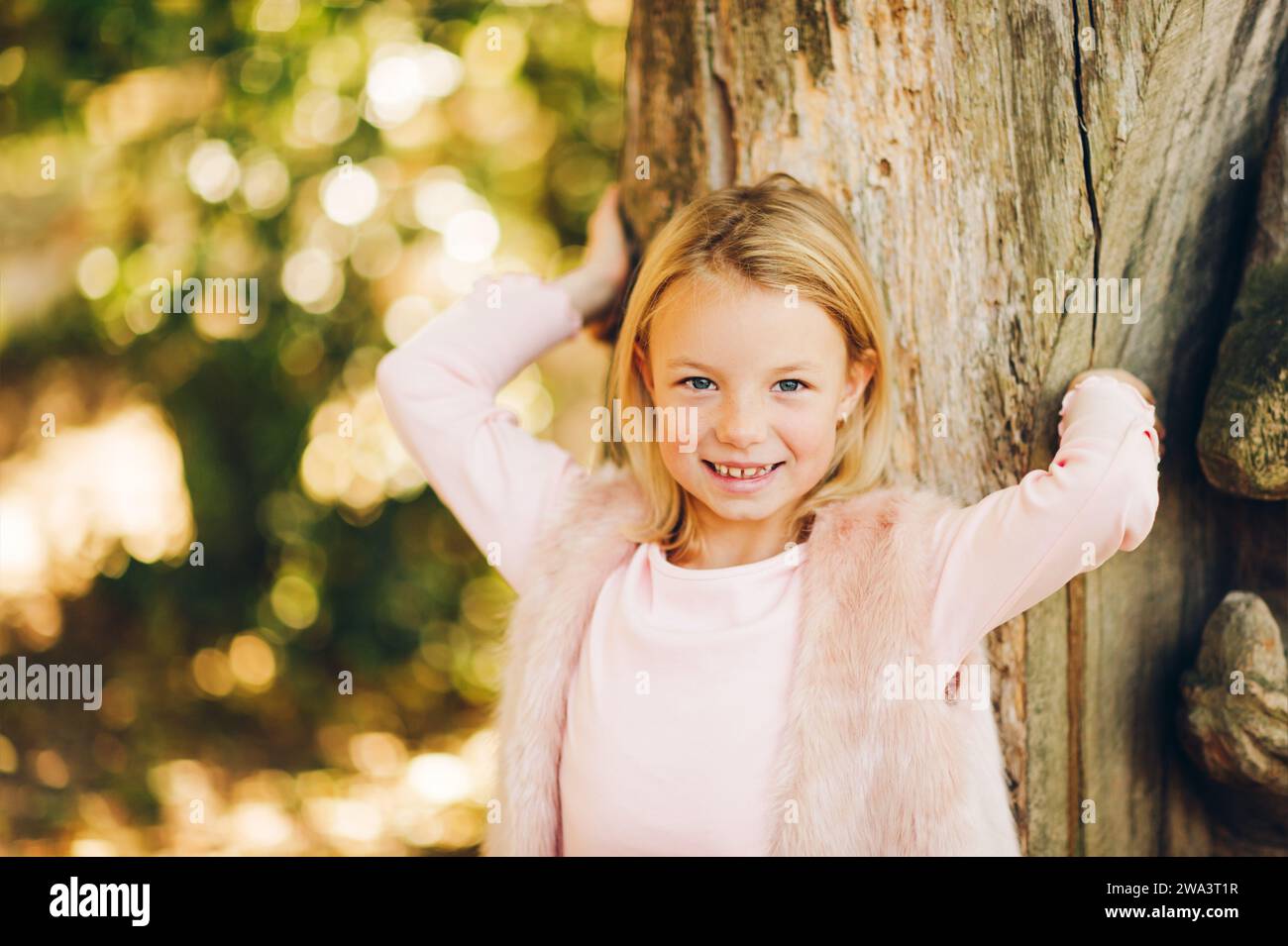 Außenporträt eines bezaubernden 7-jährigen Mädchens, blondes Haar, blaue Augen, rosafarbene Kleidung Stockfoto