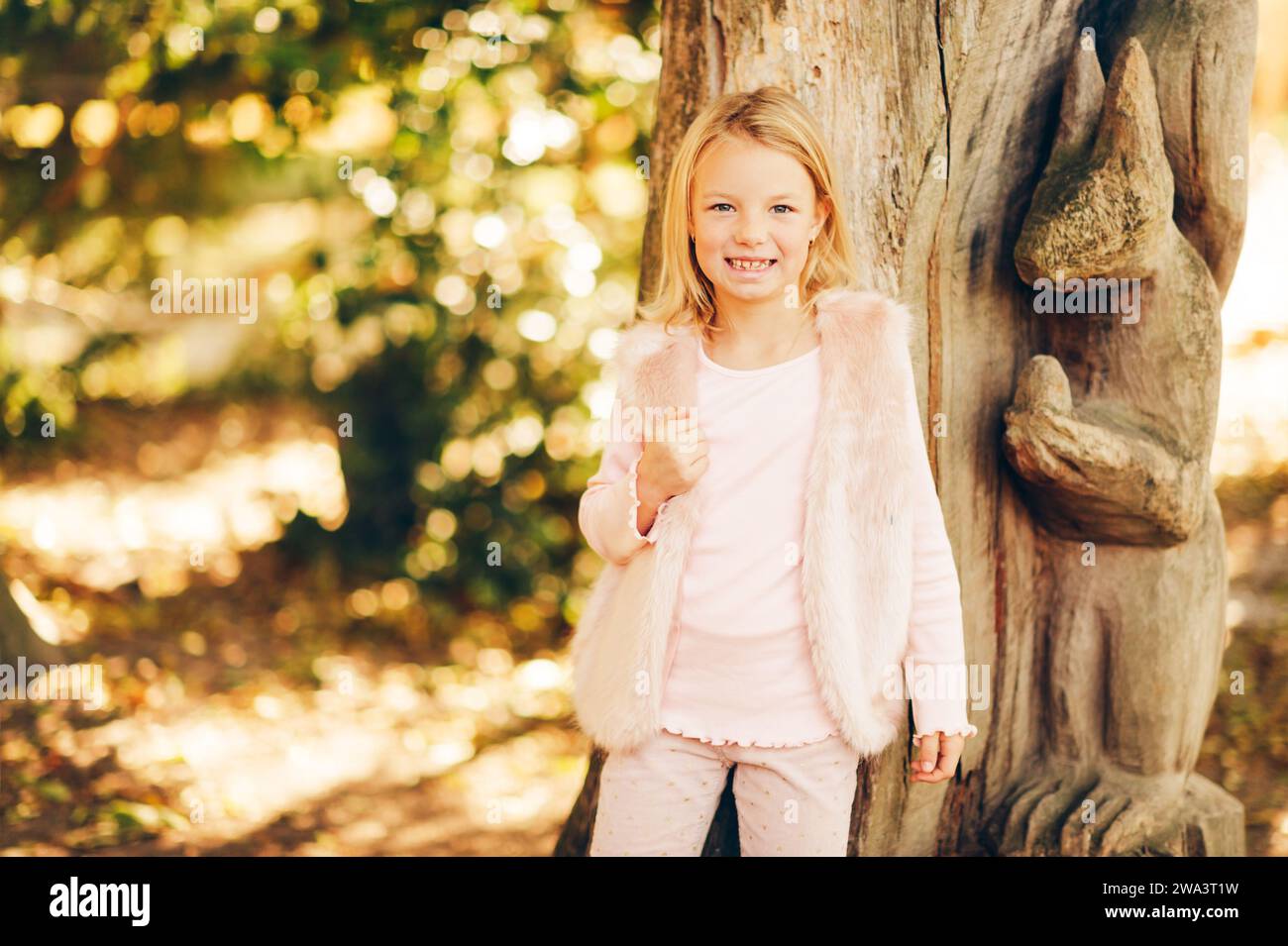 Außenporträt eines bezaubernden 7-jährigen Mädchens, blondes Haar, blaue Augen, rosafarbene Kleidung Stockfoto