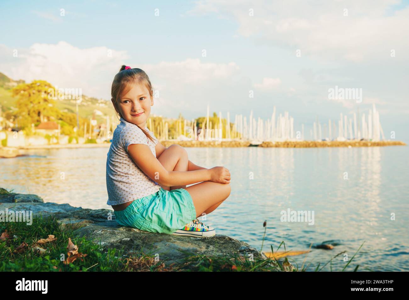 Süßes kleines Mädchen, das an einem schönen, sonnigen, warmen Abend am See ausruht Stockfoto